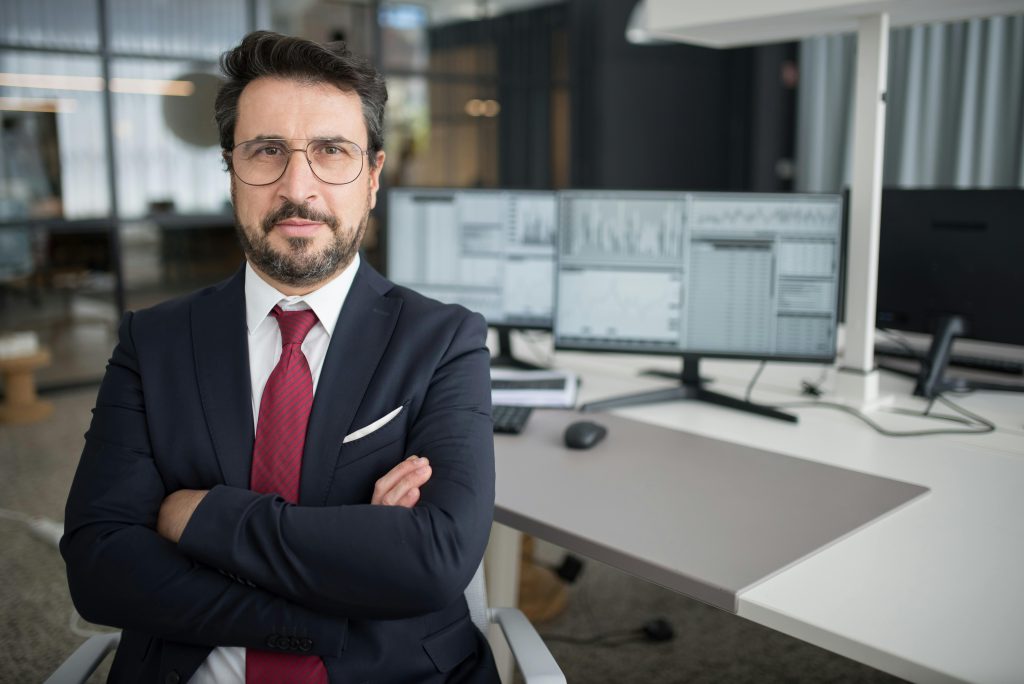 Business professional in corporate attire with arms crossed in a modern office space.